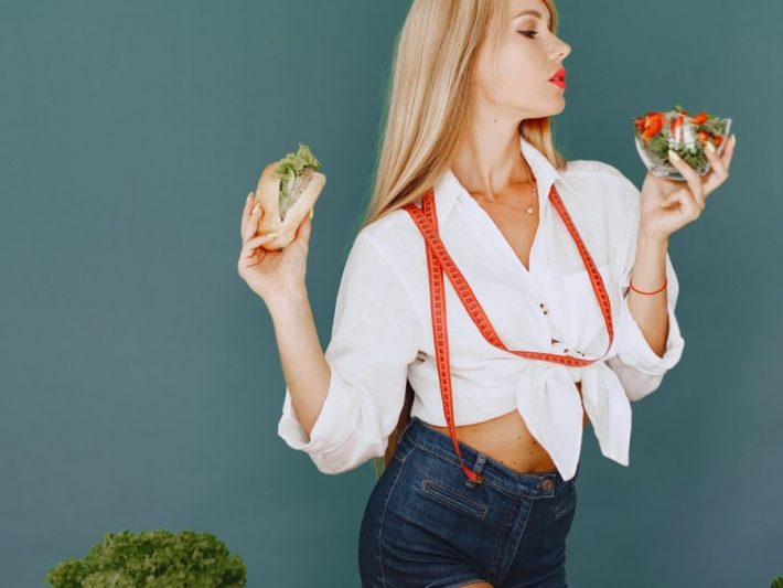 Woman enjoys healthy lifestyle with fresh salad and sandwich, promoting balanced eating.